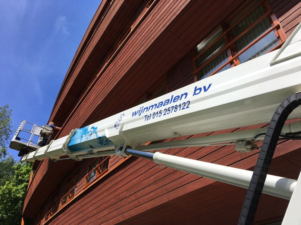 Arm van een hoogwerker van Wijnmaalen bv langs een rode houten gevel
