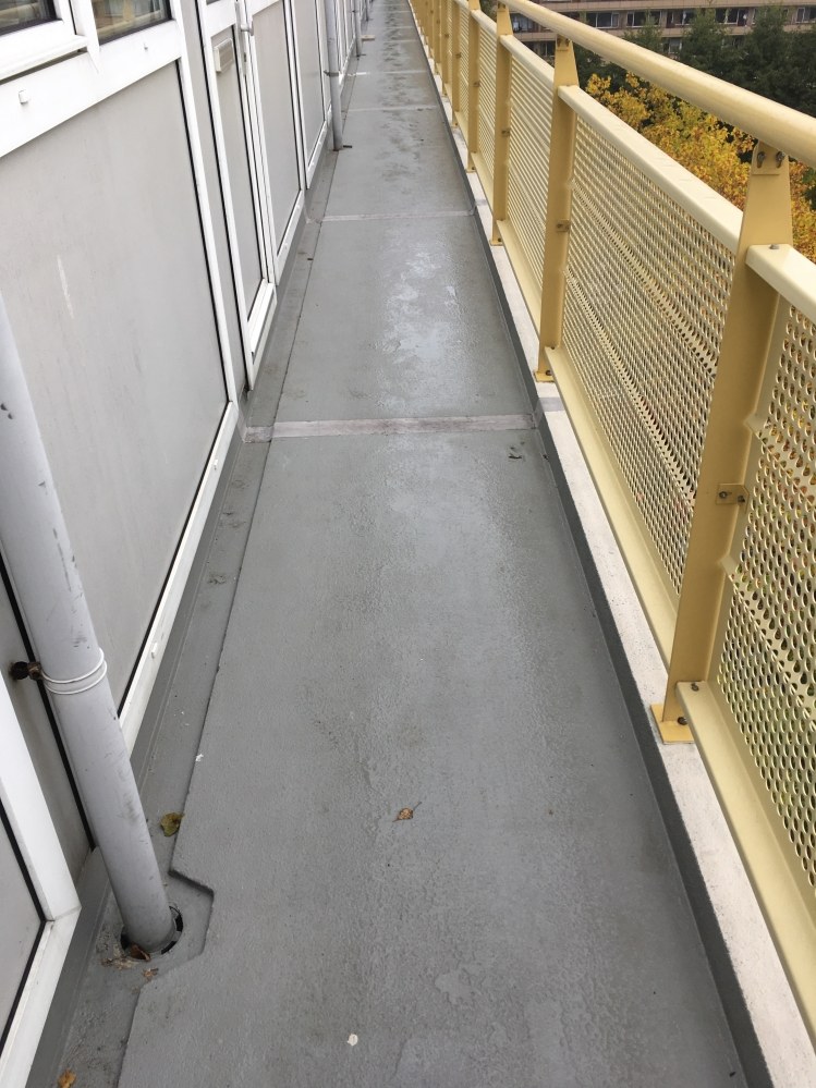 Schoongemaakte galerij met grijze vloer en een gele geperforeerde balustrade