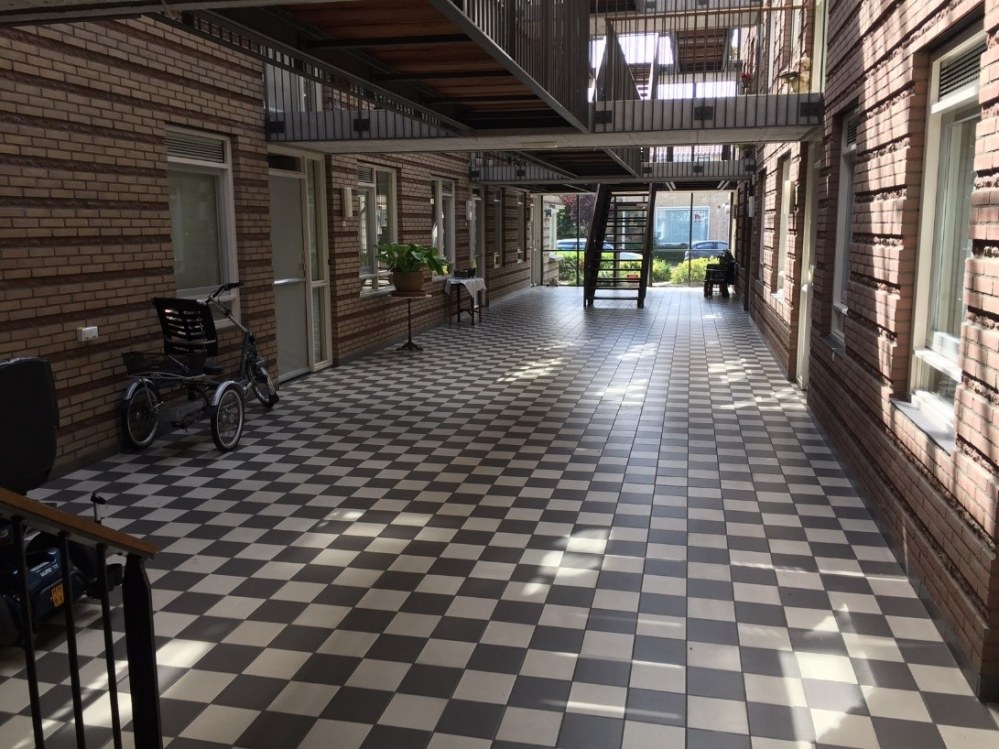 Binnengalerij van een woongebouw met geblokte tegelvloer en trappen