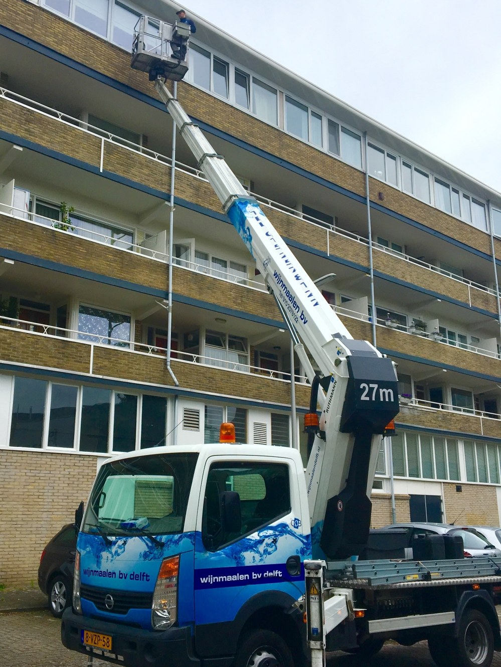 Bedrijfsbus met hoogwerker naast een flatgebouw voor het wassen van ramen