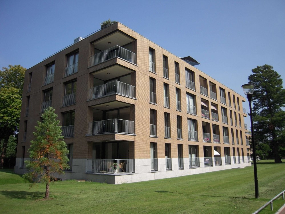 Appartementencomplex van lichte baksteen met balkons, gazon en bomen